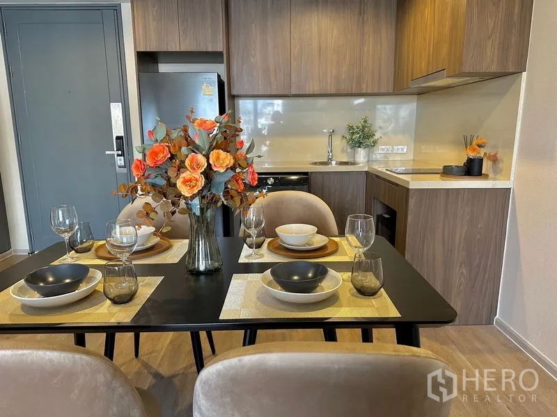 Condominium for rent in Pathum Wan, Bangkok - Dining table set for four next to a wood-finished kitchenette with upper cabinets.