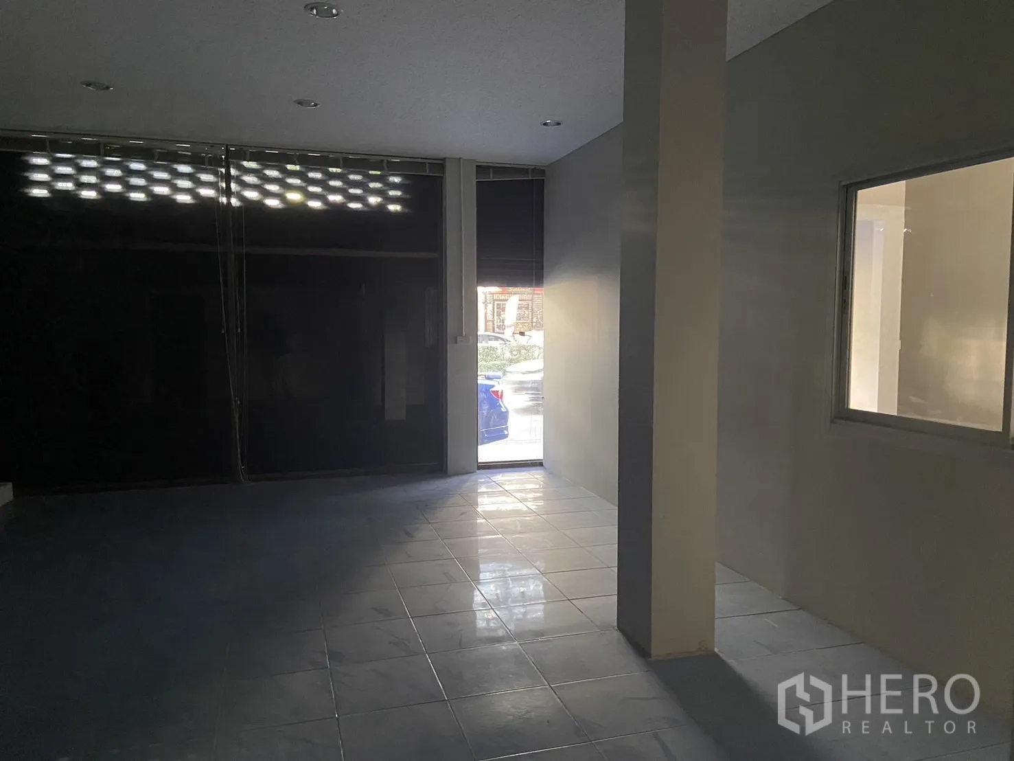 Shophouse for rent in Bang Na, Bangkok - Front retail space with tiled floor and a partially open roller door allowing daylight.