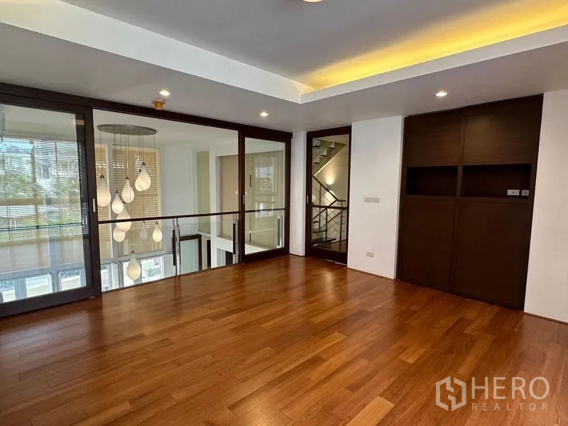 Townhouse for sale in Yan Nawa, Bangkok - Upper living area with wood floors, glass partitions and statement pendant lights overlooking a double-height space.