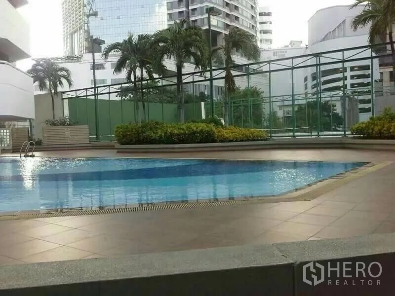 Condominium for rent in Watthana, Bangkok - Outdoor swimming pool with tiled deck, planters and city buildings in the background.