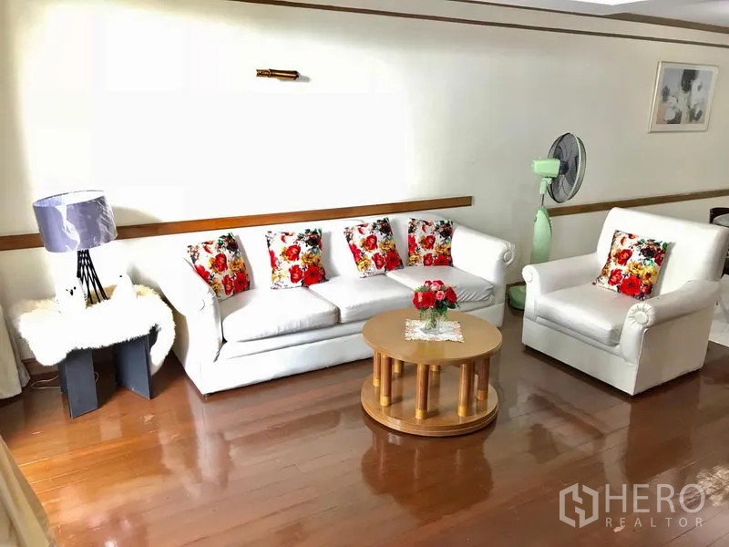 公寓 出租在Watthana, Bangkok - 明亮会客角，白色沙发与花色抱枕，圆形茶几与木地板。