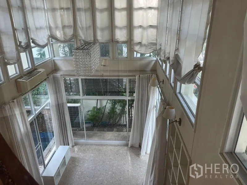 Detached House for rent or sale in Khan Na Yao, Bangkok - Double-height living room with full-height windows, sheer curtains and a chandelier overlooking the garden.