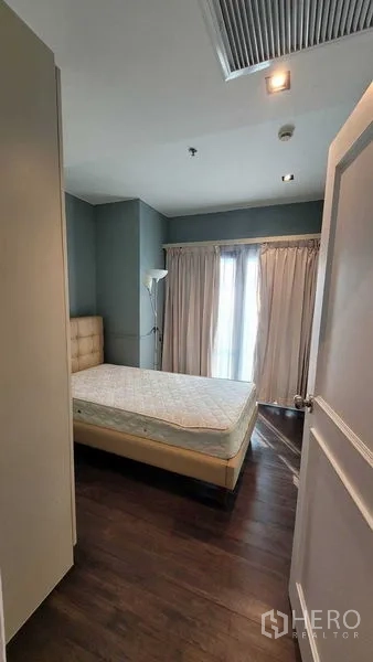 Condominium for rent in Khlong Toei, Bangkok - Compact bedroom with wardrobe, balcony doors, teal walls and wooden flooring.