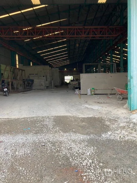 Warehouse for rent in Mueang Samut Sakhon, Samut Sakhon - Deep warehouse aisle with overhead red truss and materials stacked inside.