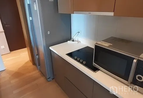 Condominium for rent in Khlong Toei, Bangkok - Compact galley kitchen featuring induction hob, built-in storage and a side-by-side fridge.