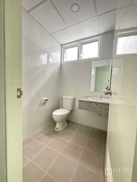 Factory for rent in Khlong Luang, Pathum Thani - Clean restroom with white tiles, toilet and vanity beneath small windows.