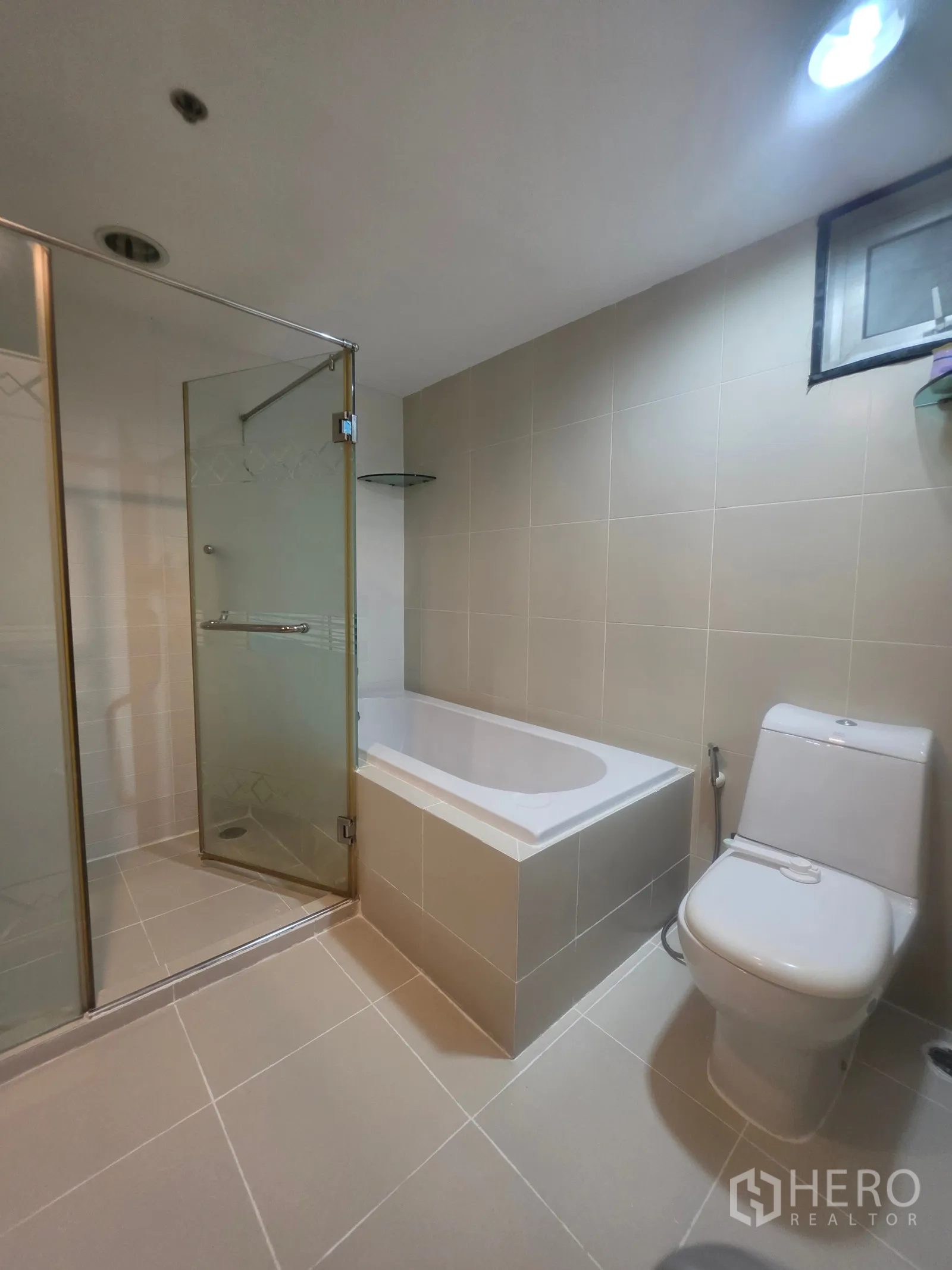 Condominium for rent in Huai Khwang, Bangkok - Bathroom showing bathtub, toilet, and frosted glass shower doors.