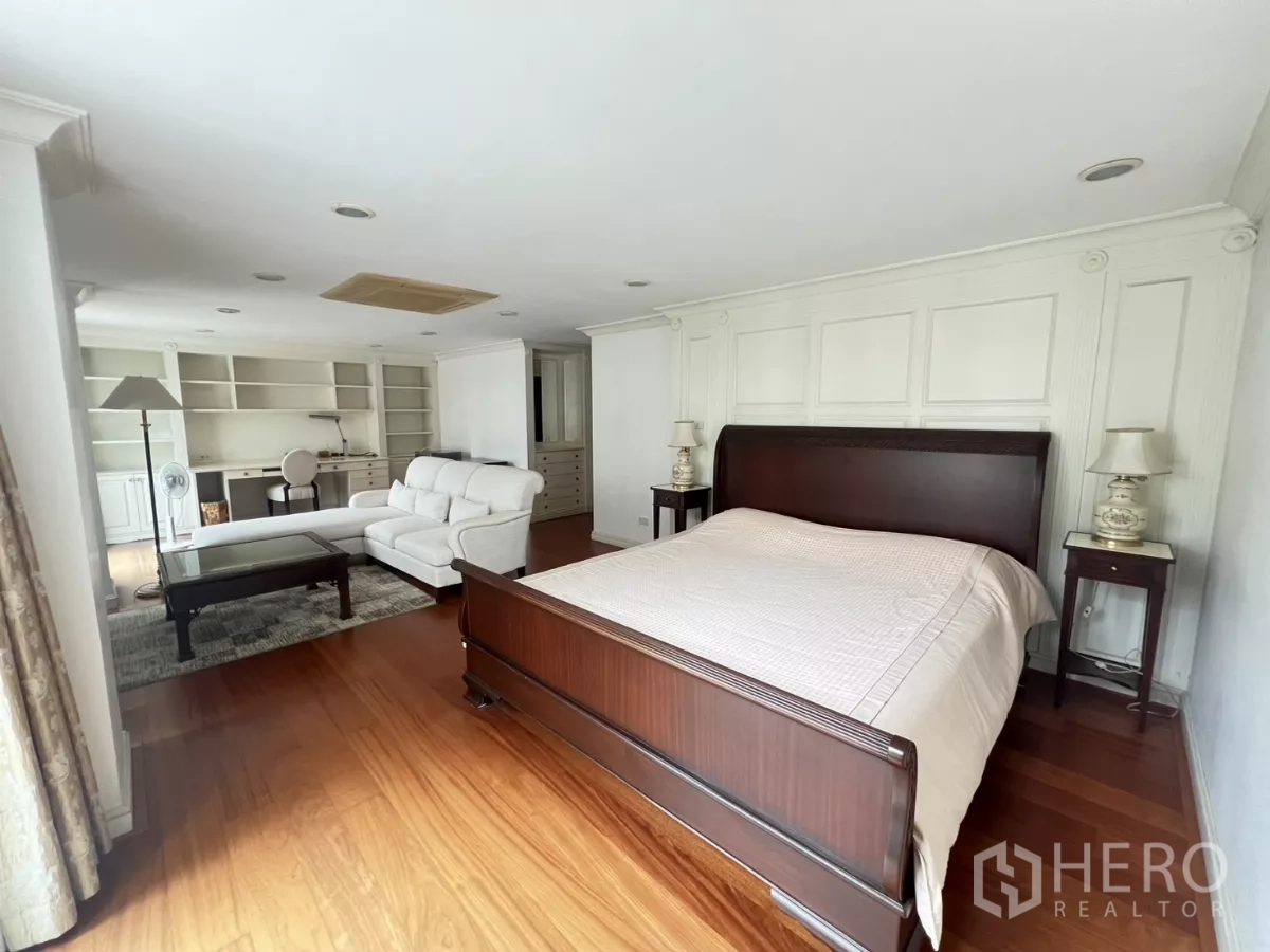 Townhouse for sale in Watthana, Bangkok - Spacious master bedroom with wooden bed, sitting area and built-in shelving.