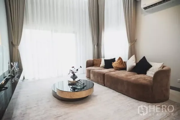 独立式住宅 出租在Bang Phli, Samut Prakan - 通透明亮的起居区，落地纱帘、柔软沙发与圆形玻璃茶几。