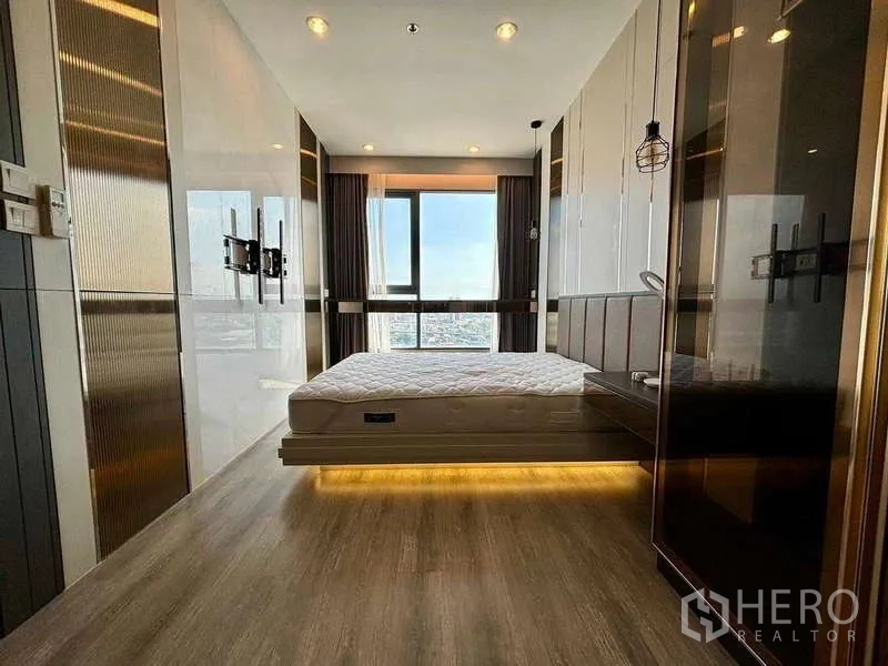 Condominium for rent or sale in Bang Na, Bangkok - Front view of the master bedroom showing a city-view window, pendant lights and sleek wall panels.