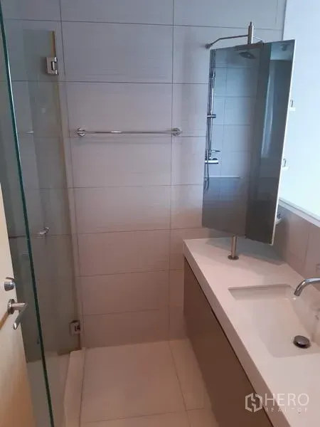 Condominium for rent in Khlong Toei, Bangkok - Clean bathroom with glass shower enclosure, long vanity and wall mirror