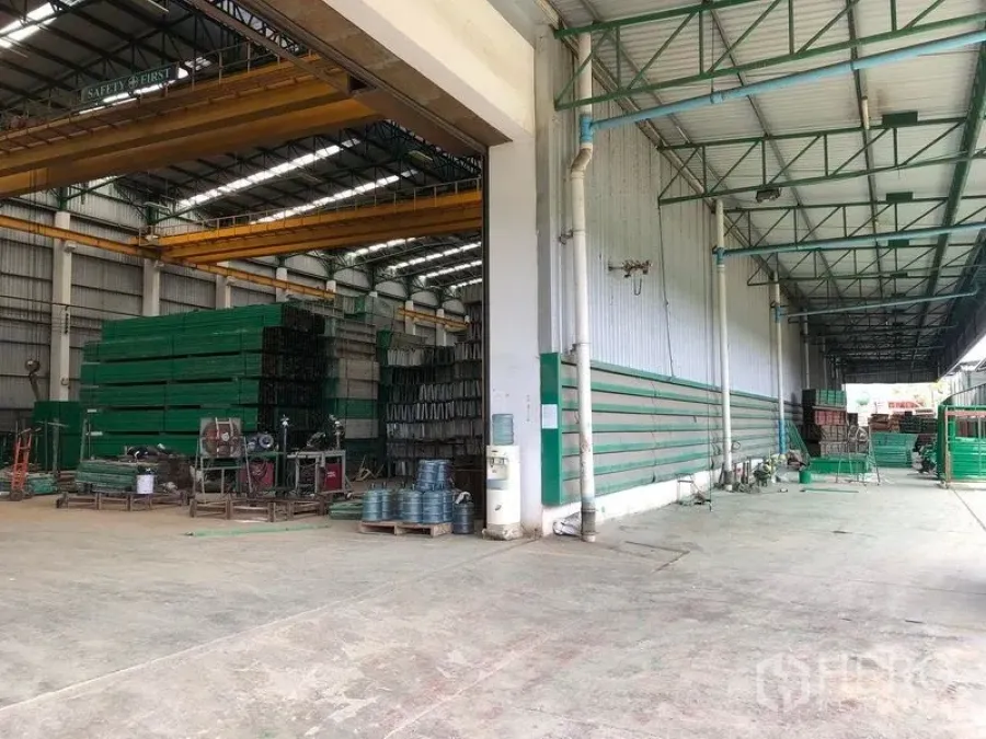 Factory for rent or sale in Lat Lum Kaeo, Pathum Thani - Spacious factory warehouse with high roof, overhead cranes and stacked green materials beside a covered loading bay.