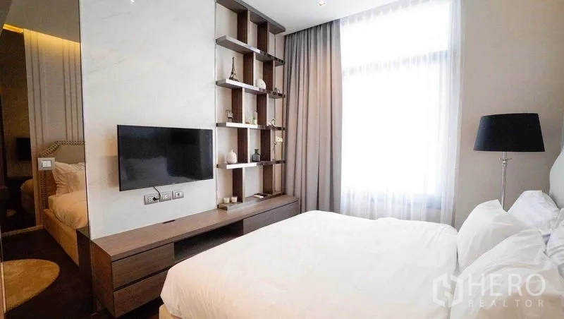 Condominium for sale in Watthana, Bangkok - Bright bedroom with mounted TV, open shelving and large curtained window in a modern condo.