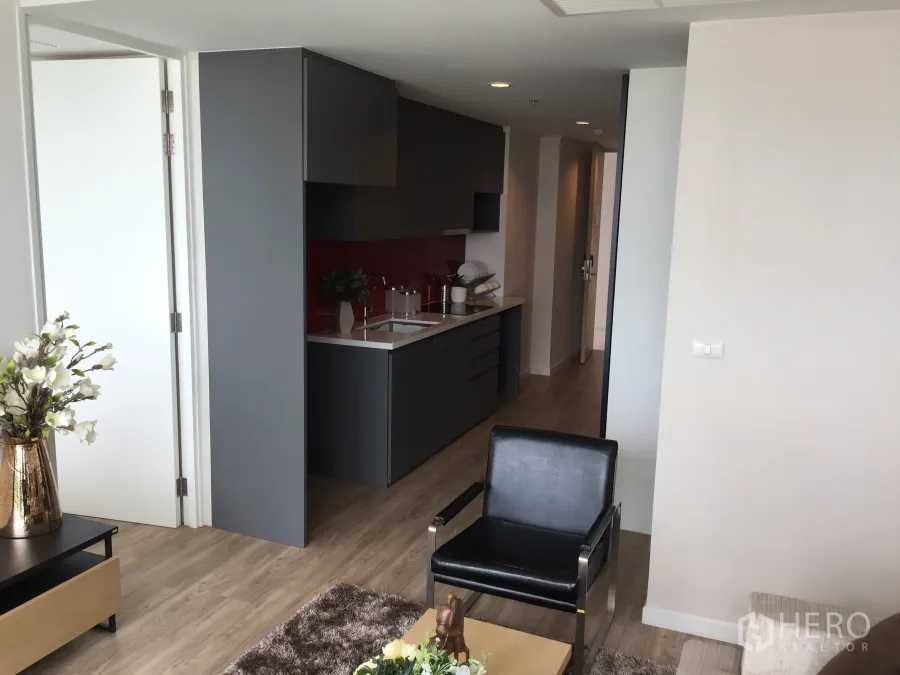 Condominium for sale in Bang Rak, Bangkok - Open-plan living area with sleek grey kitchenette, red backsplash and wood flooring at Siamese Surawong condo.