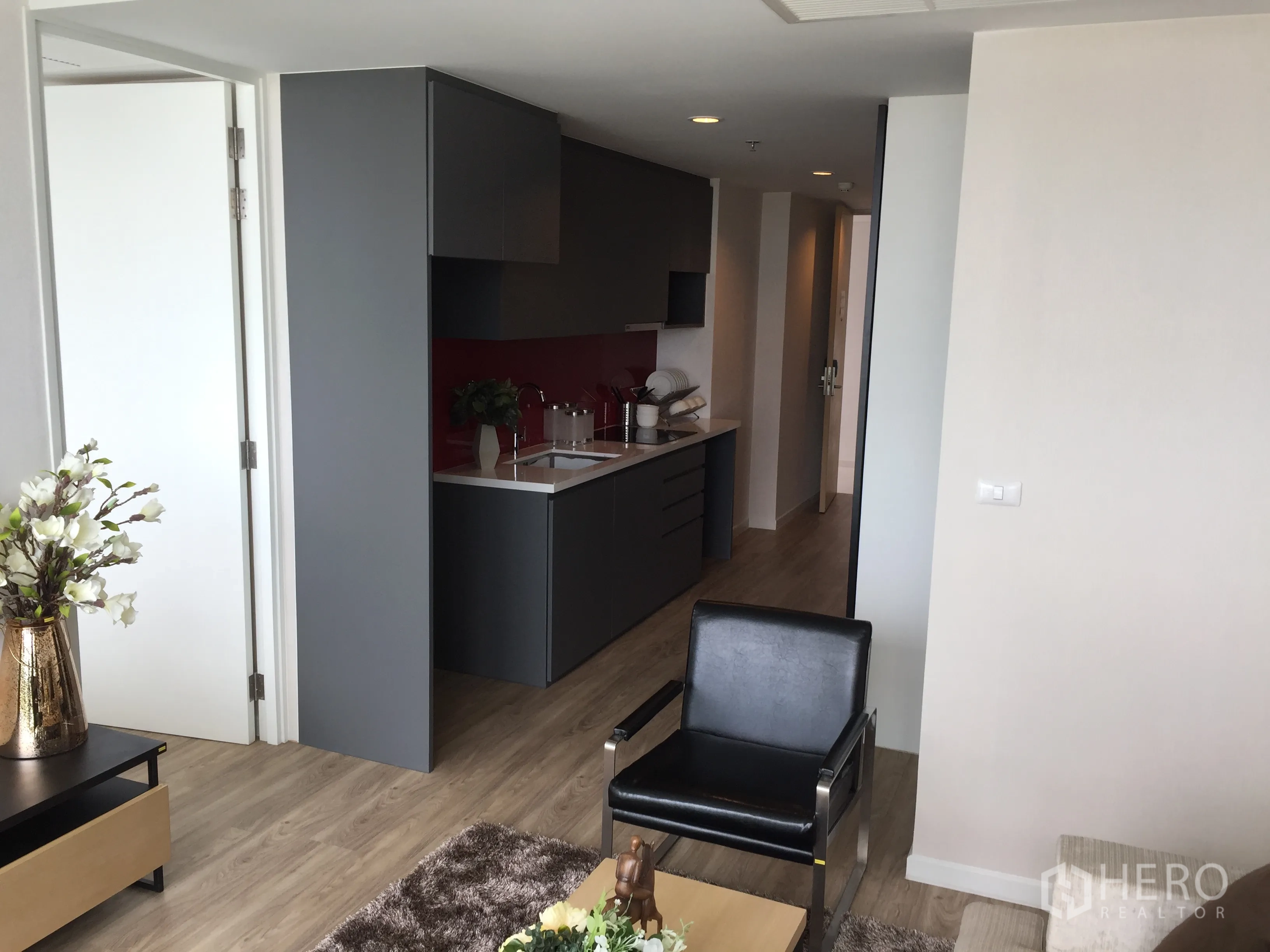 Condominium for sale in Bang Rak, Bangkok - Open-plan living area with sleek grey kitchenette, red backsplash and wood flooring at Siamese Surawong condo.