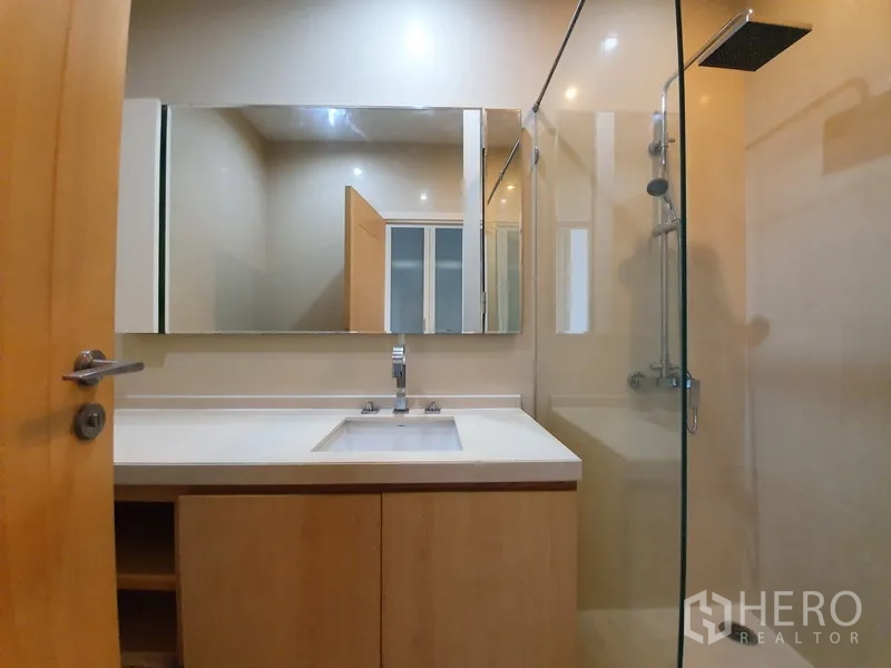 Condominium for rent in Chatuchak, Bangkok - Modern bathroom with wide vanity, large mirror and glass-enclosed shower.