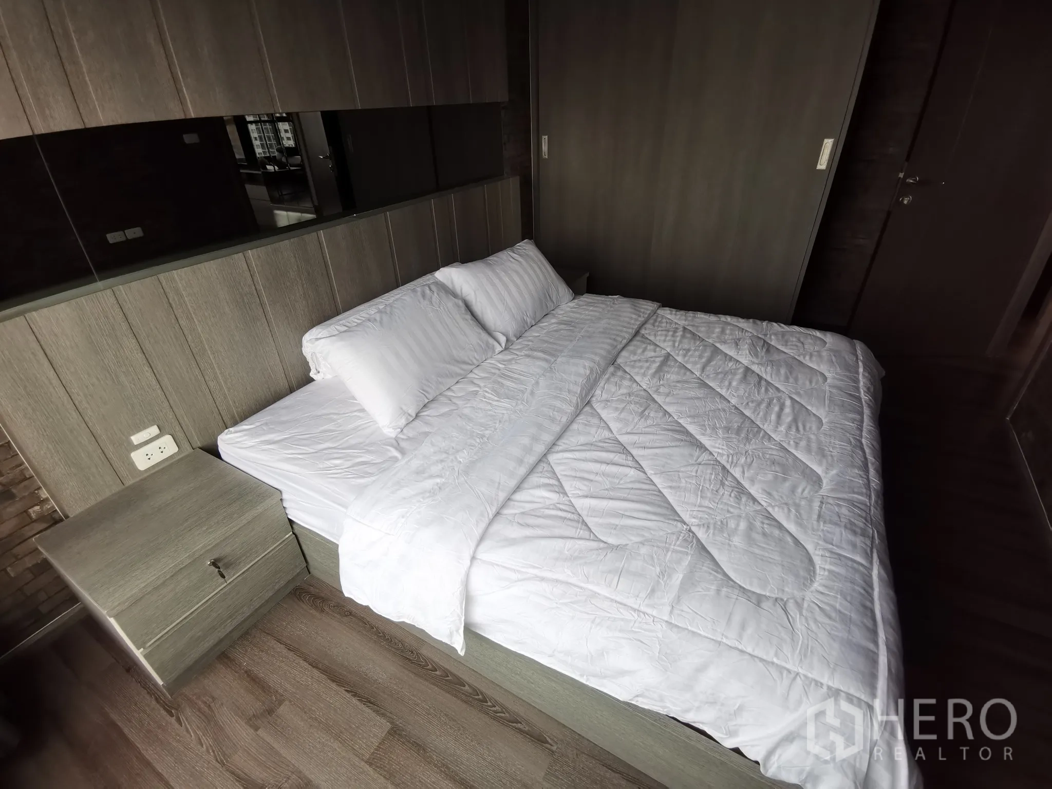 Condominium for rent or sale in Watthana, Bangkok - Master bedroom with king bed, bedside table and wood panel feature wall.