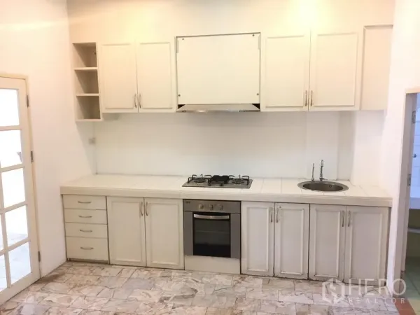 Townhouse for rent in Chatuchak, Bangkok - Built-in white kitchen featuring gas hob, oven, range hood and ample upper and lower cabinets.