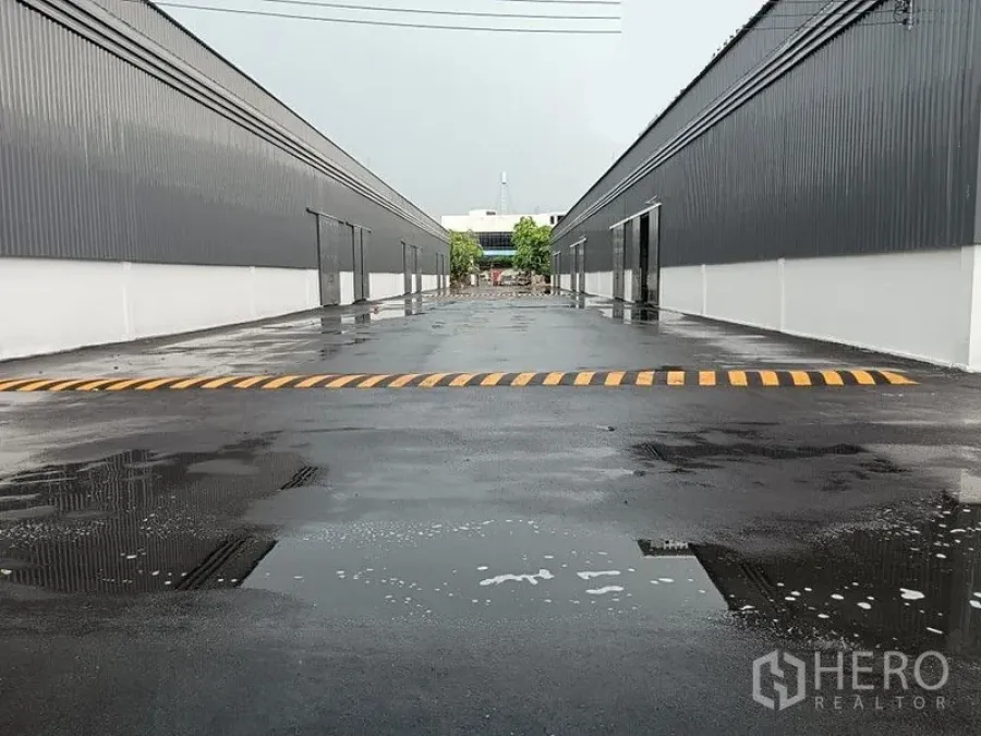 Warehouse for rent in Khlong Toei, Bangkok - Central driveway through the warehouse compound with reflective wet surface and a speed hump.