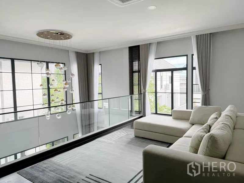 Detached House for rent or sale in Bang Phli, Samut Prakan - Upstairs family lounge with glass balustrade, sectional sofa and pendant lighting.