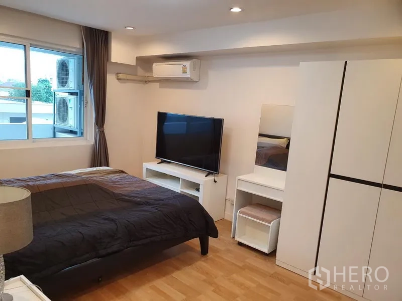 Condominium for rent in Watthana, Bangkok - Master bedroom with double bed, TV on console, wardrobe, vanity, and window air-conditioning.