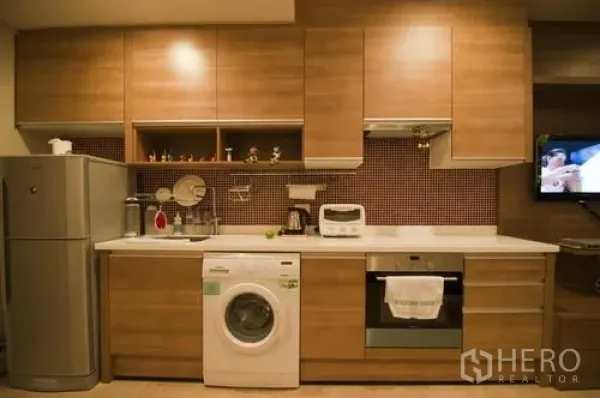 Condominium for rent in Khlong Toei, Bangkok - Fitted kitchen with wood cabinets, refrigerator, oven, cooktop, and in-unit washing machine.