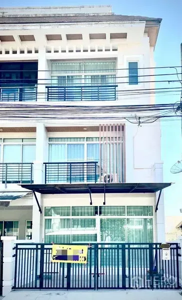 Townhouse for rent in Prawet, Bangkok - Three-storey modern townhouse facade with balconies, awning and gated carport.