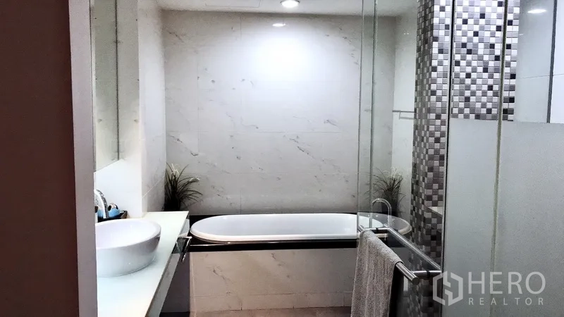 Condominium for rent in Bang Rak, Bangkok - Modern bathroom featuring a soaking bathtub, glass shower and marble-look tiles.