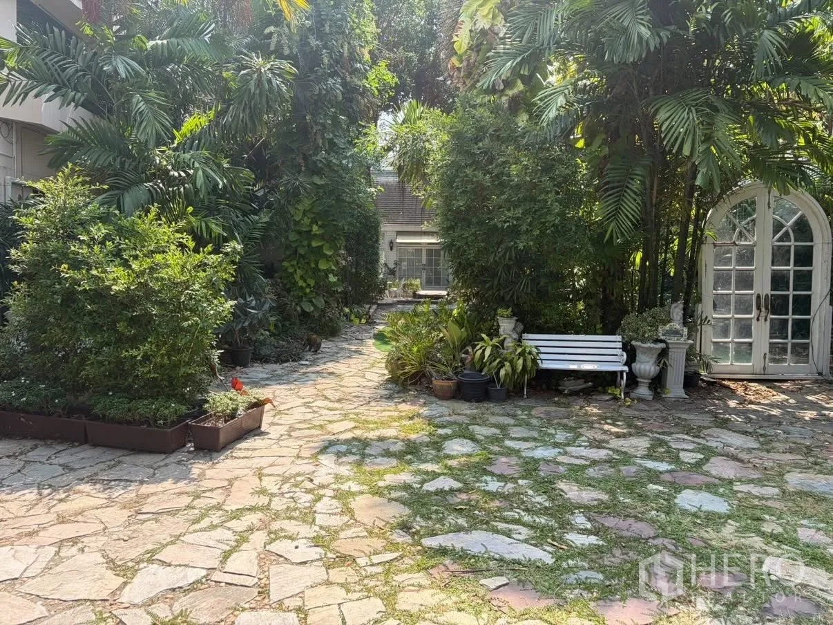 Detached House for rent in Phra Khanong, Bangkok - Garden path with a white bench and arched glass doors framed by greenery.