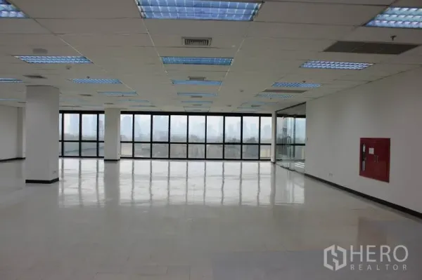 办公空间 出租在Watthana, Bangkok - 开放式办公室，整面落地窗，城市与公园湖景，网格吊顶照明与亮面地坪。