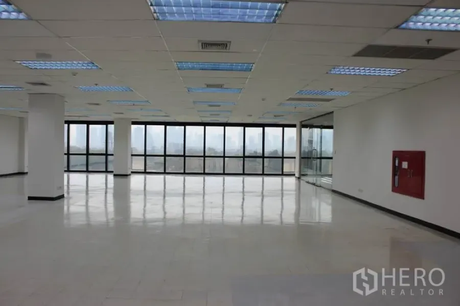 办公空间 出租在Watthana, Bangkok - 开放式办公室，整面落地窗，城市与公园湖景，网格吊顶照明与亮面地坪。