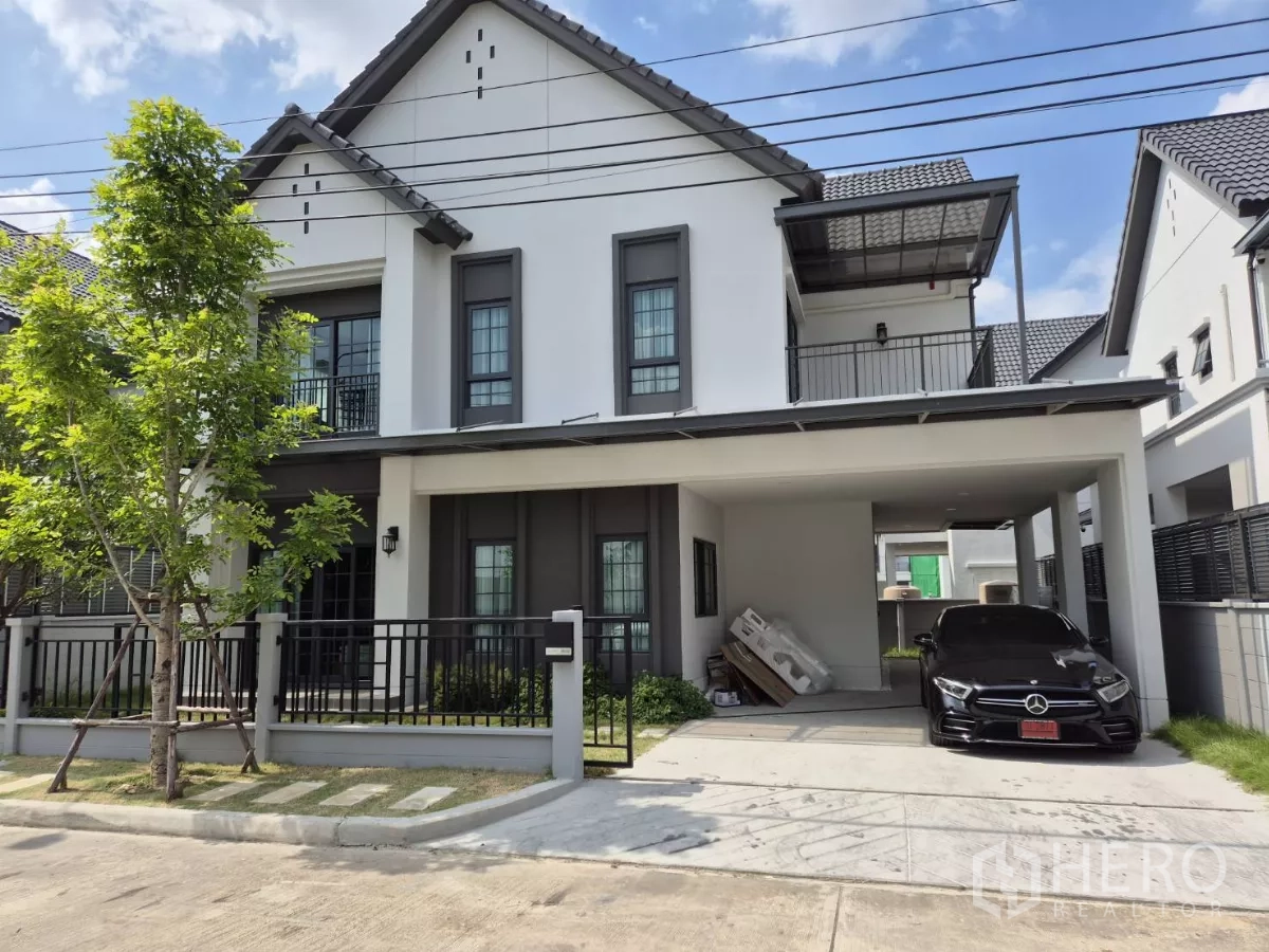 独立式住宅 出租在Bang Phli, Samut Prakan - 两层现代独栋别墅外观，带前院围栏、阳台与双车位遮雨车棚。