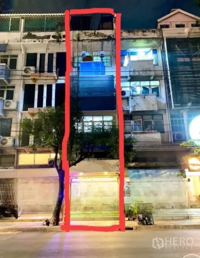 Shophouse for rent in Watthana, Bangkok - Multi‑storey shophouse exterior highlighted at night on a busy street.