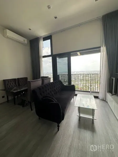 Condominium for rent in Phra Khanong, Bangkok - Bright living room with high ceiling, floor-to-ceiling windows and a balcony overlooking the Bangkok skyline.