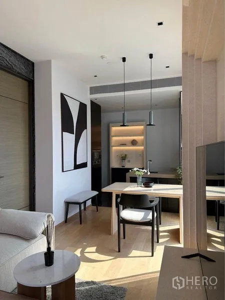 Condominium for rent in Pathum Wan, Bangkok - Minimalist dining space with pendant lighting, modern artwork and a compact kitchen behind.