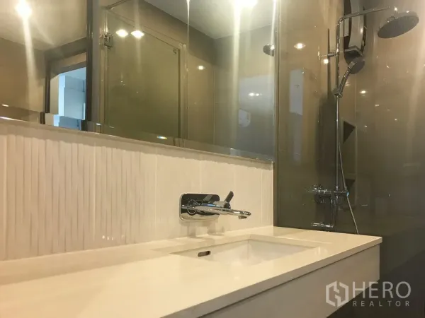 Condominium for sale in Khlong Toei, Bangkok - Contemporary bathroom featuring a glass shower with rain showerhead and a sleek vanity sink.