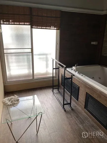 联排别墅 出租在Wang Thonglang, Bangkok - 浴室设大尺寸按摩浴缸，旁有磨砂窗与小玻璃桌