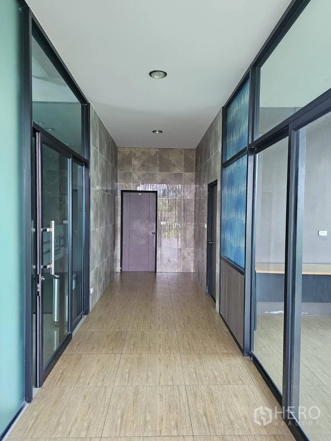 Warehouse for rent in Lam Luk Ka, Pathum Thani - Tiled corridor with glass partitions and doors inside the office building.