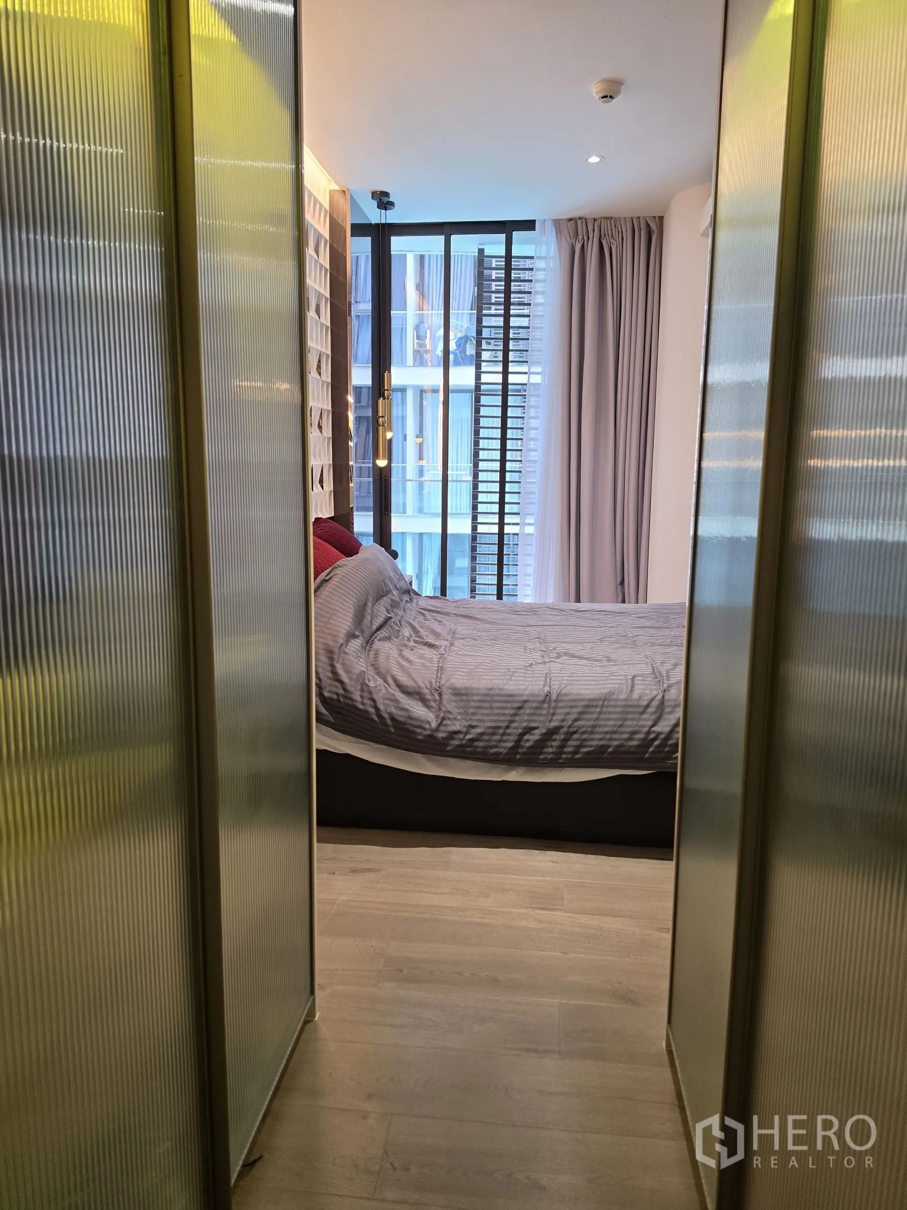 Condominium for rent in Khlong Toei, Bangkok - Hallway with frosted-glass wardrobes leading to a bedroom with floor-to-ceiling windows.