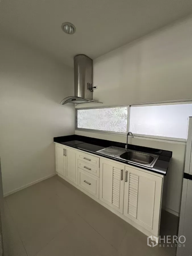 Townhouse for rent in Suan Luang, Bangkok - Compact kitchen with white cabinets, black countertop, and a range hood.