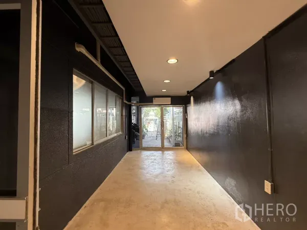 办公空间 出租在Wang Thonglang, Bangkok - 入口走廊，黑色墙面、嵌灯和通往室外的推拉玻璃门。