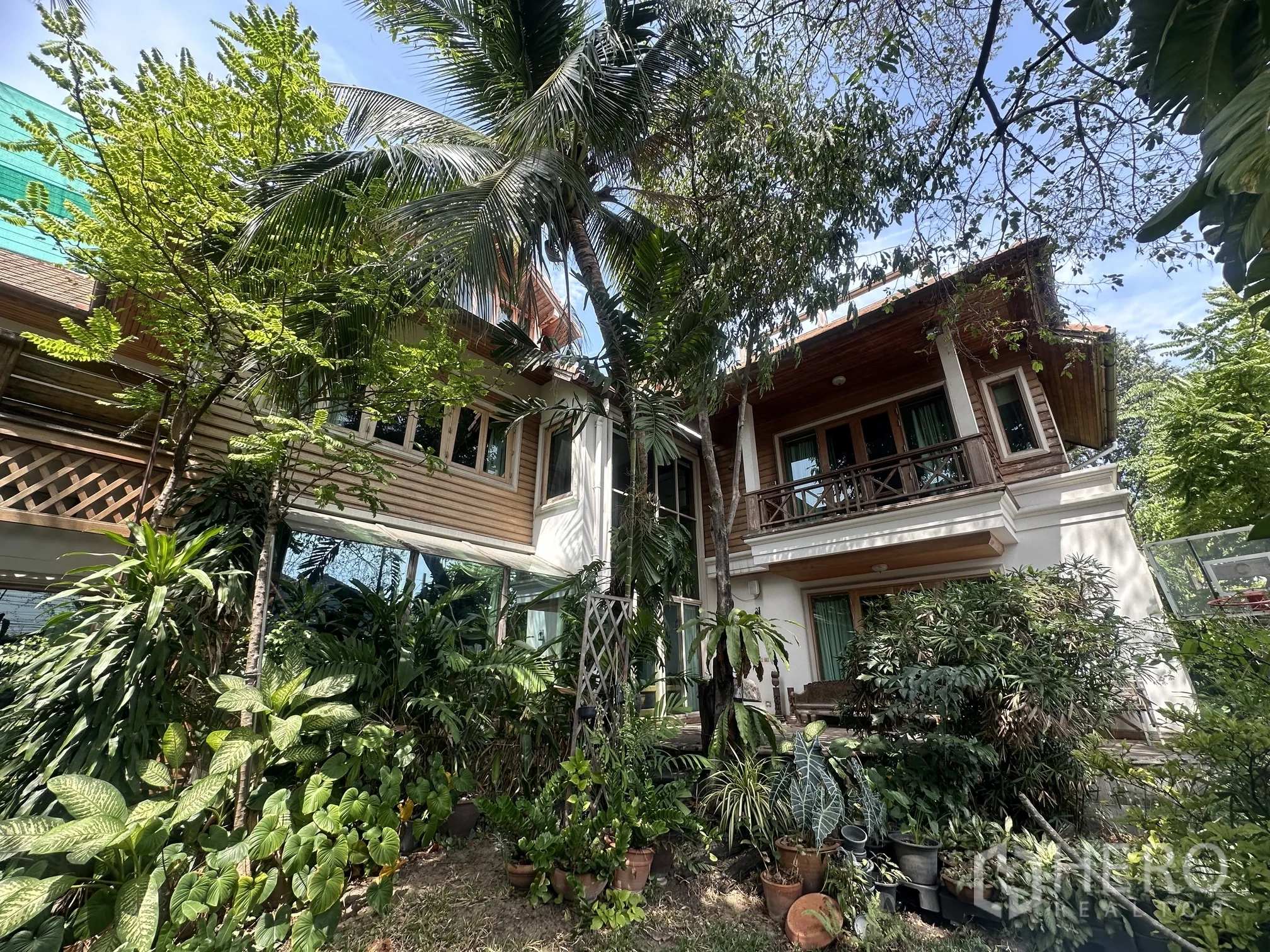 Detached House for rent in Lam Luk Ka, Pathum Thani - Lush tropical garden surrounding a two-storey detached house with wooden balconies.