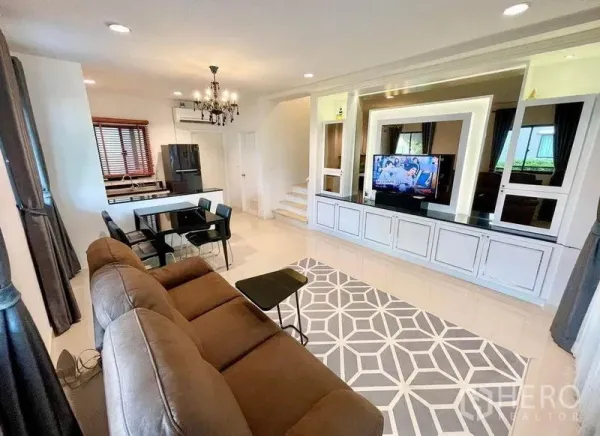 Townhouse for sale in Wang Thonglang, Bangkok - Open-plan living and dining area with sofa, chandelier, TV and an adjoining kitchen with breakfast bar.