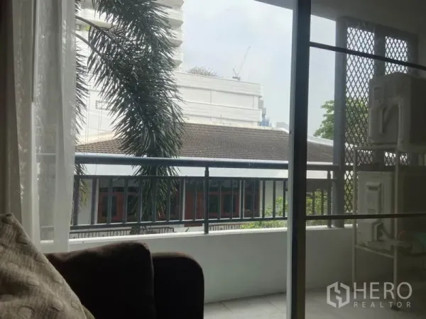 公寓 出租在Watthana, Bangkok - 私家阳台，可眺望棕榈树与附近低层建筑，金属栏杆安全稳固。