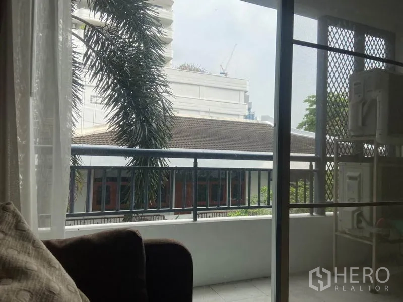 公寓 出租在Watthana, Bangkok - 私家阳台，可眺望棕榈树与附近低层建筑，金属栏杆安全稳固。