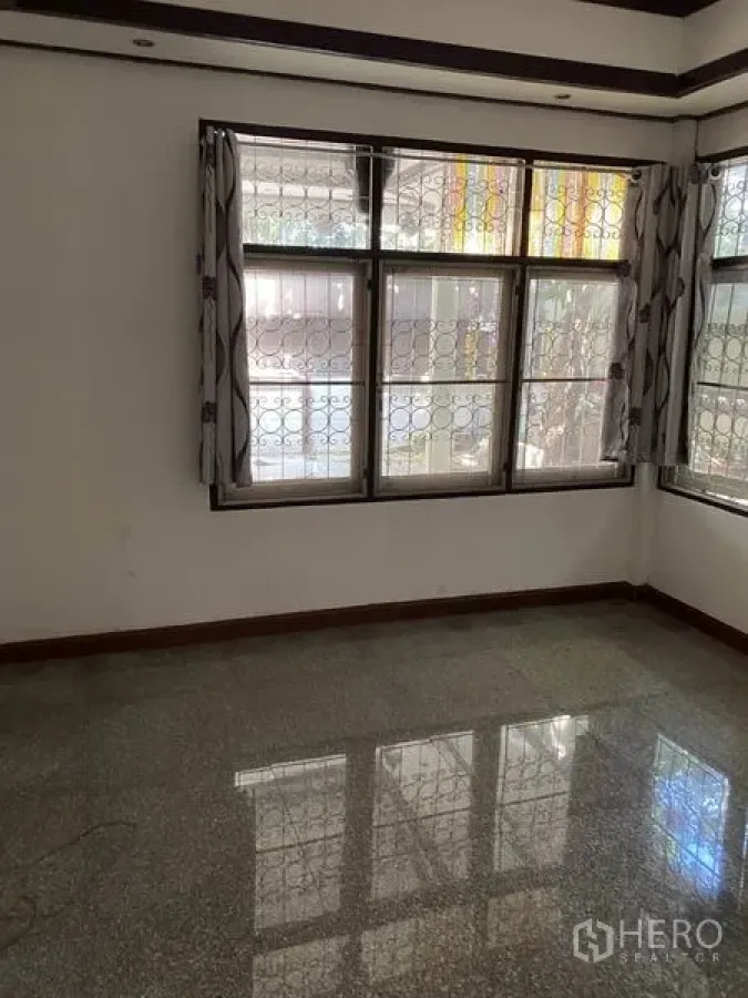 Townhouse for rent in Lat Phrao, Bangkok - Sunlit bedroom with corner windows, curtains, and polished stone flooring.