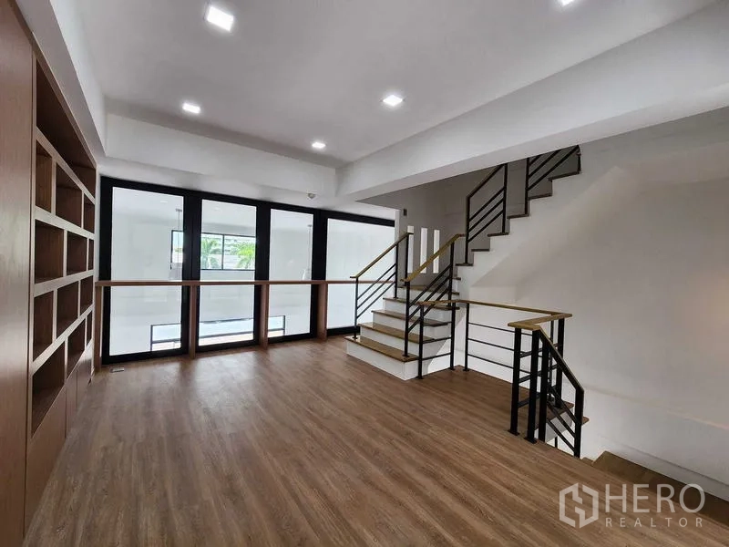 带办公室的家 出租在Prawet, Bangkok - 楼梯平台设有内建书柜，大片窗户与金属木质楼梯相连。