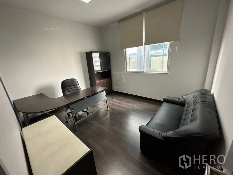 Office Space for rent in Khlong Toei, Bangkok - Private office room with executive desk, cabinet, window blinds and a black sofa on dark wood flooring.