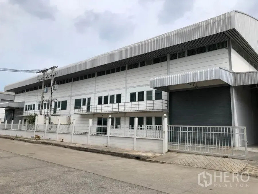 工厂 出租在Lam Luk Ka, Pathum Thani - 两层现代工厂外观，金属板立面、围栏与大型卷闸门，临安静道路
