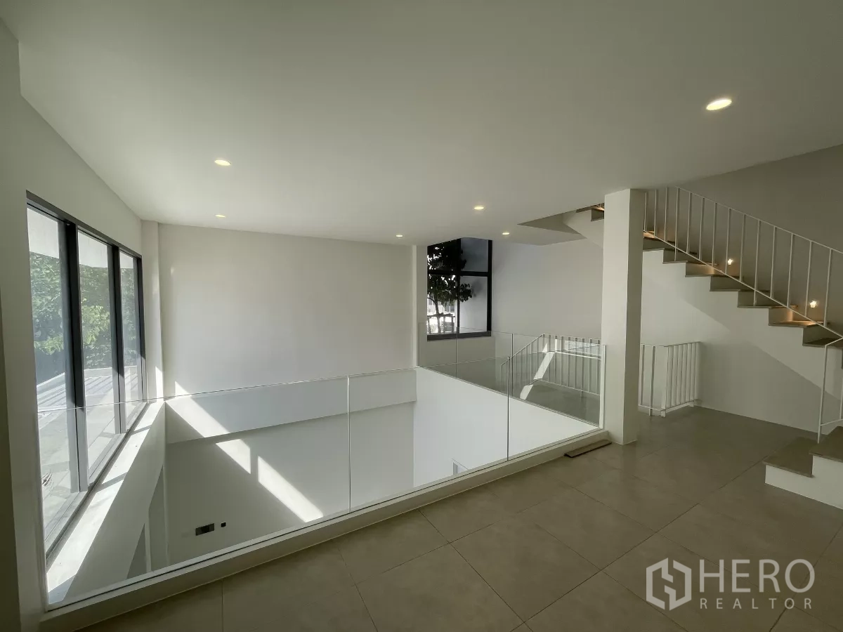 Home Office for rent in Don Mueang, Bangkok - Upper landing with glass balustrade beside staircase and wide windows.